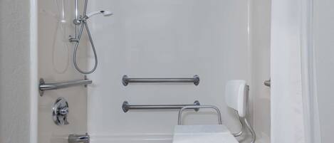 A white bathtub with a handheld showerhead, grab bars, and a handheld soap dispenser.