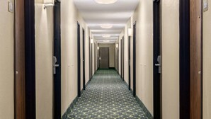 Et hotelkoryssar med et mønstret tæppe, døre på begge sider og en lampe i loftet.