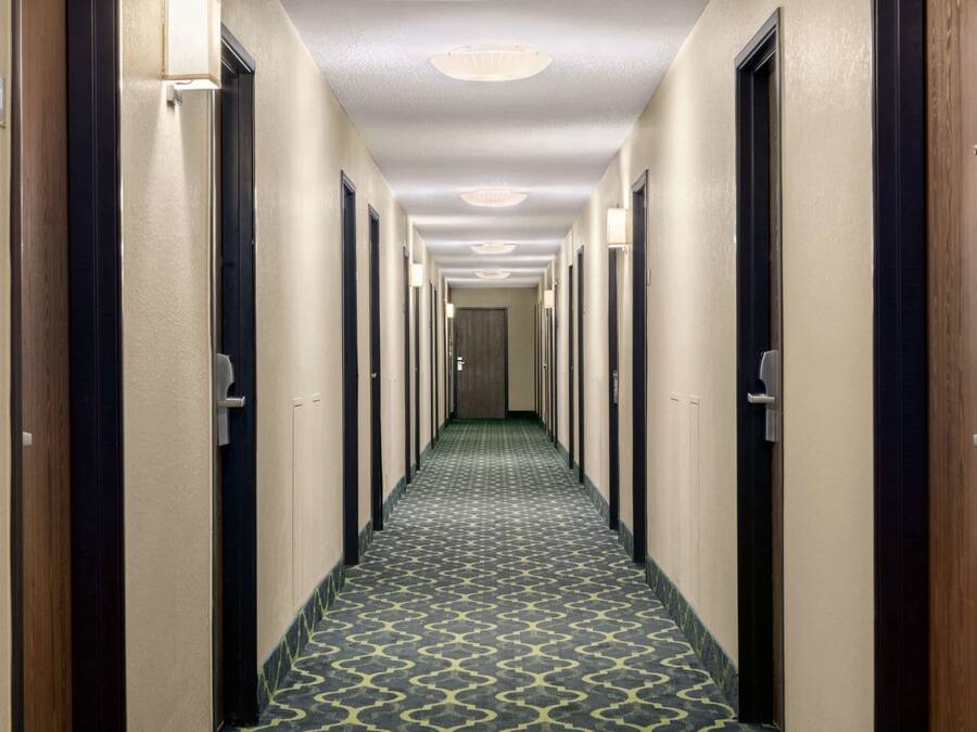 A hotel hallway with a patterned carpet, doors on both sides, and a light fixture on the ceiling.