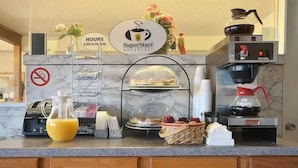 A hotel breakfast counter with a SuperStart sign, a no-smoking sign, a coffee machine, and a juice dispenser.