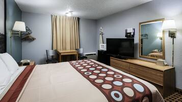 A hotel room with a bed, a desk, a television, a mirror, and a wall-mounted lamp.