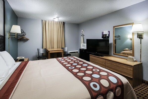 A hotel room with a bed, a desk, a television, a mirror, and a wall-mounted lamp.