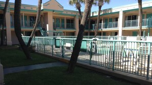 A hotel with a two-story building, a fenced courtyard, and palm trees.