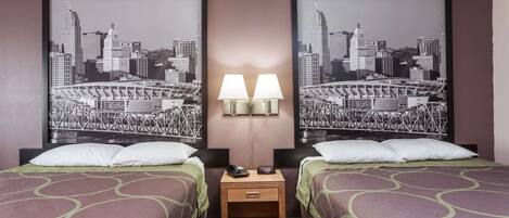 Une chambre d’hôtel avec deux lits, une table de chevet avec une lampe et deux tableaux représentant des paysages urbains, accrochés au mur.