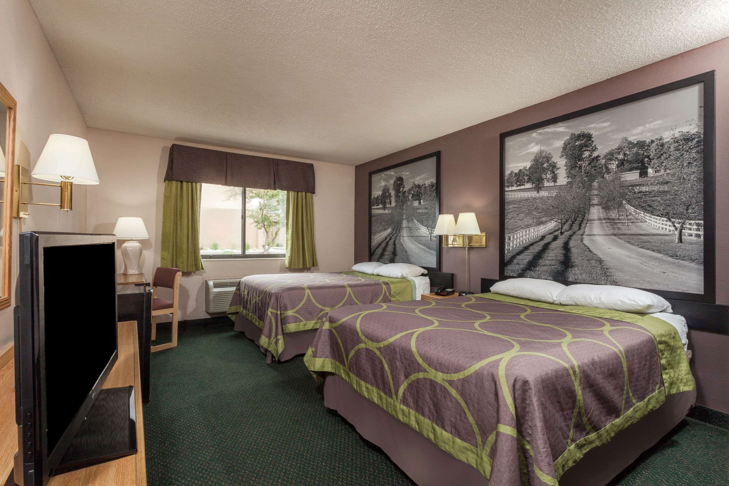 A hotel room with two beds, a television, and a large framed picture on the wall.