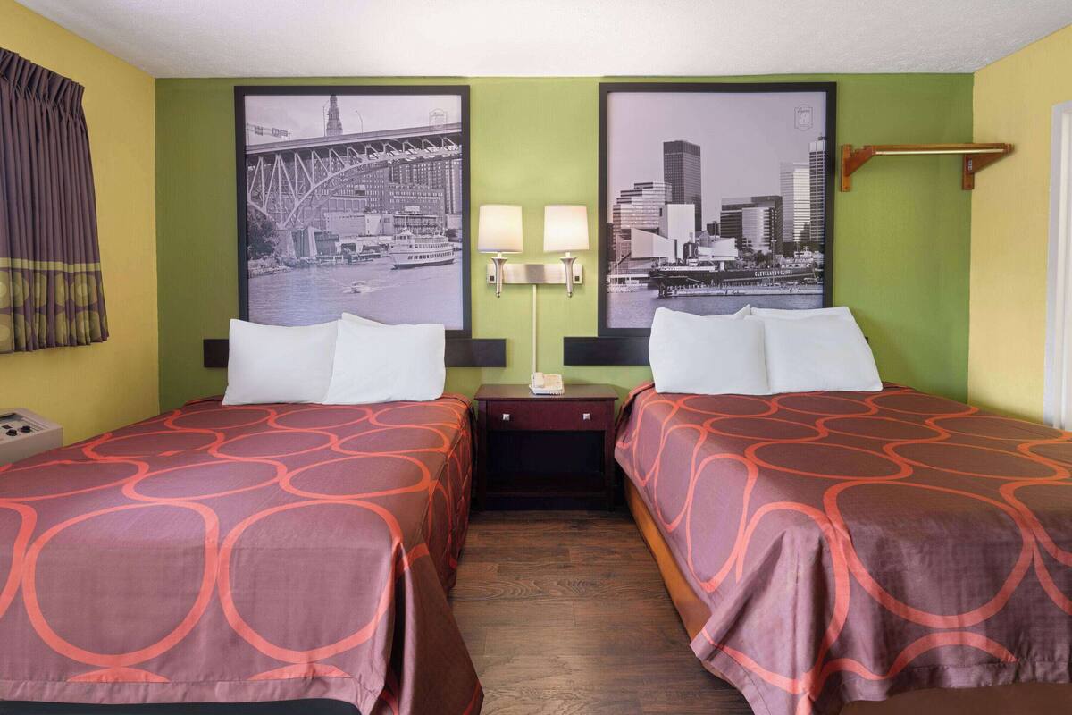 A hotel room with two beds, green walls, and cityscape pictures on the wall.