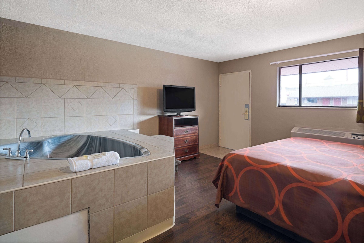 A hotel room with a bathroom, a bed, a television, and a window.
