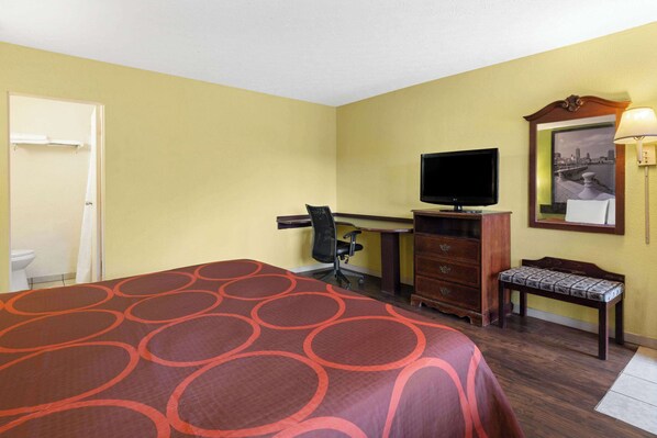 A hotel room with a bed, a desk with a computer, a television, a chair, a bench, and a mirror.