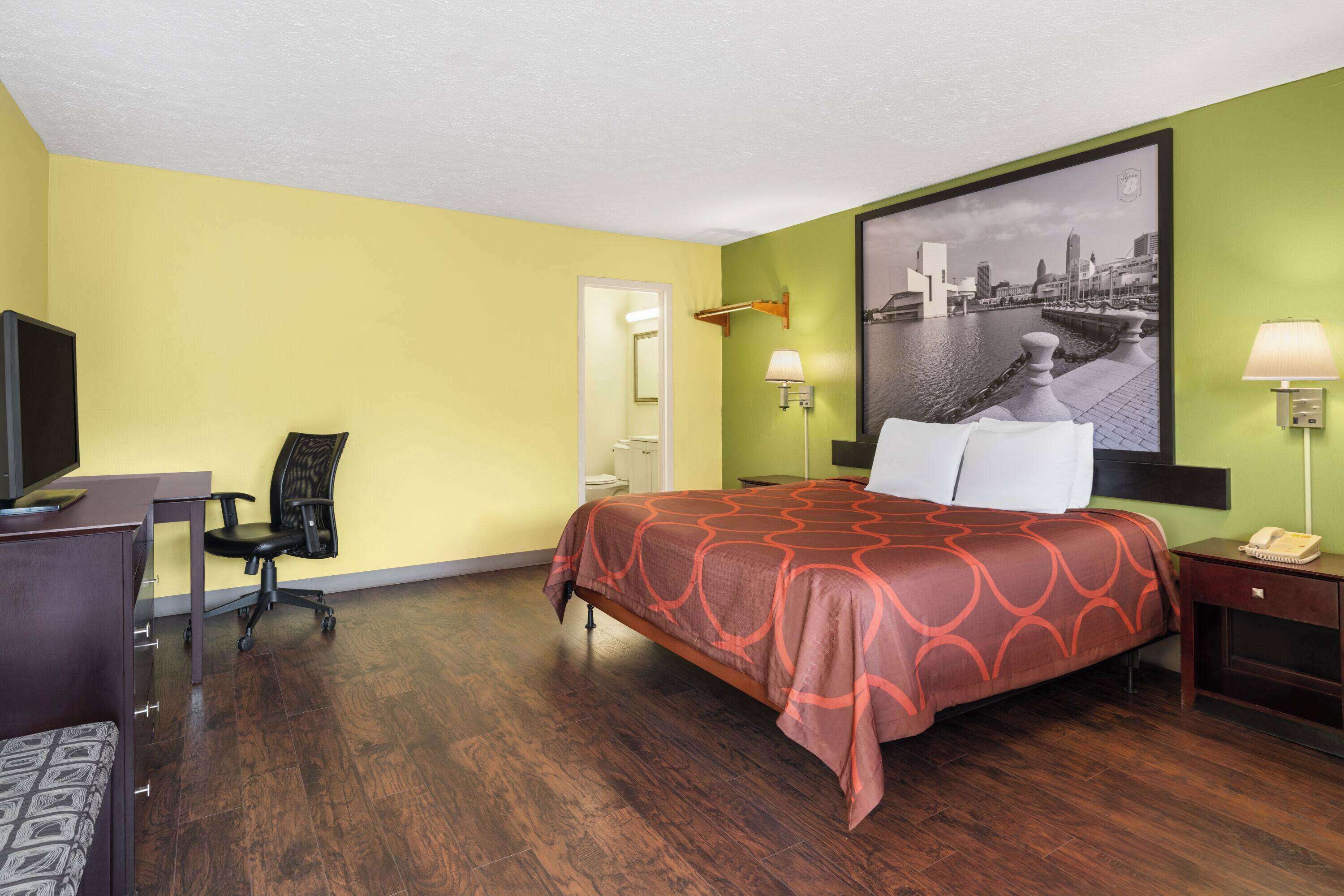 Habitación de hotel con cama, escritorio, silla y un cuadro de paisaje urbano en la pared.