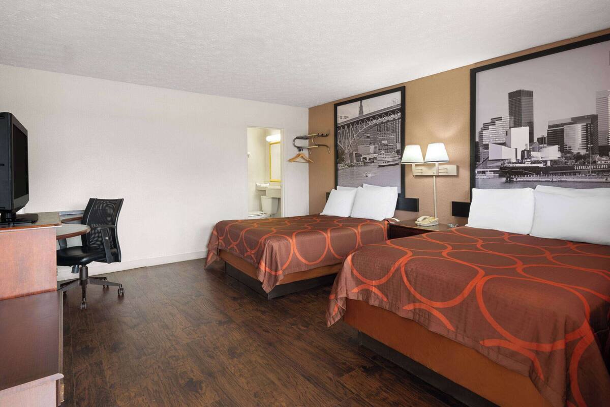 A hotel room with two beds, a desk, a chair, a TV, and a cityscape poster on the wall.