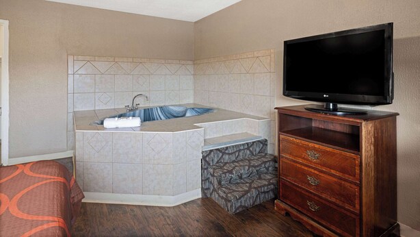 A hotel room with a small bathroom, a TV on a wooden stand, and a bed with a patterned bedspread.
