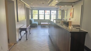 Um corredor com piso em padrão herringbone, balcão de recepção, um banco e uma placa na parede.