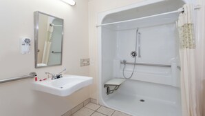 Casa de banho com lavatório, espelho e cabine de duche com barra de apoio.