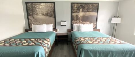 A hotel room with two beds, each with a patterned bedspread, a nightstand, and a wall-mounted lamp.