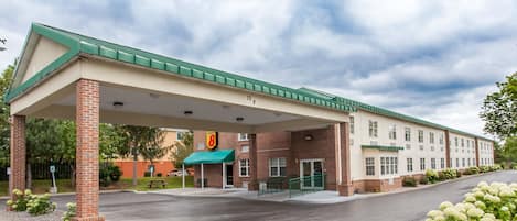 A hotel with a covered parking area, brick facade, and a green awning.