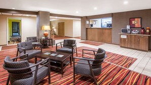 Un vestíbulo de hotel con una recepción, una estación de café y un área de estar con sillas y una mesa.