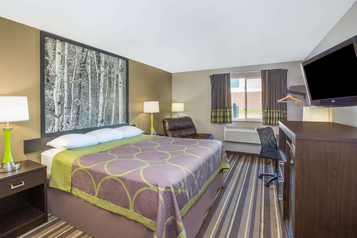 Une chambre d’hôtel avec un grand lit, deux lampes de chevet, un bureau avec une chaise, un téléviseur à écran plat et une grande fenêtre avec des rideaux.