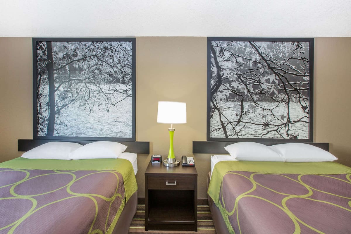 Une chambre d’hôtel avec deux lits, chacun recouvert d’une couvre-lit verte et violette, une table de chevet avec une lampe, un téléphone et un petit tiroir.