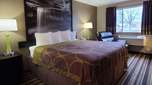 Habitación de hotel con una cama grande, dos lámparas de noche, una silla, un ventanal con cortinas y aire acondicionado de pared.