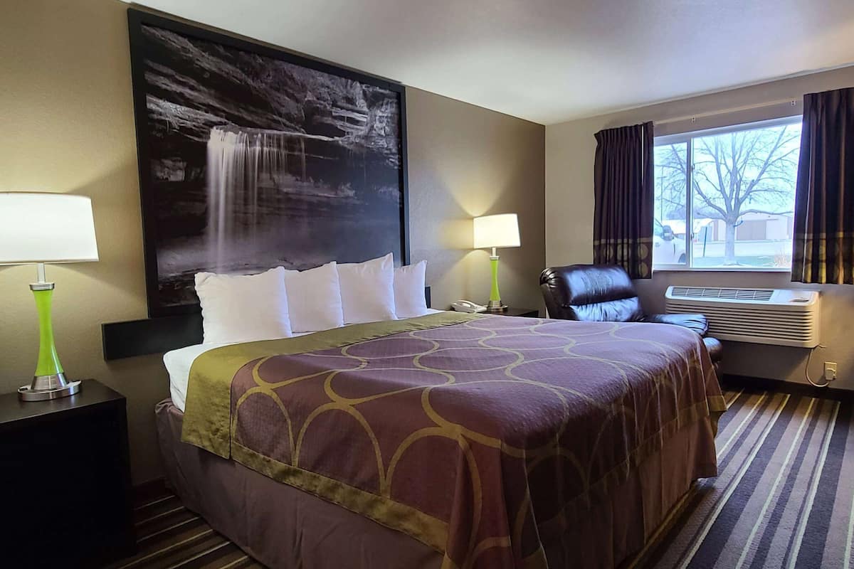 Une chambre d’hôtel avec un grand lit, deux lampes de chevet, une chaise, une fenêtre avec des rideaux et un climatiseur fixé au mur.