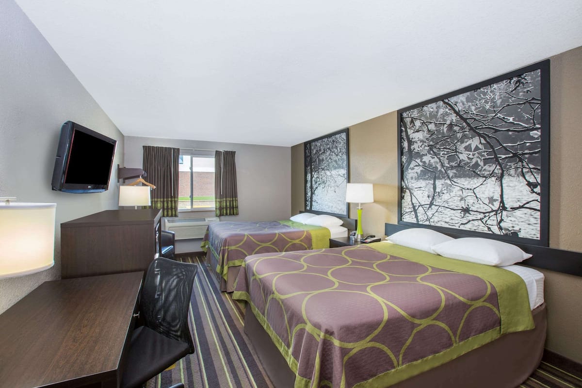 Une chambre d’hôtel avec deux lits, un bureau, une télévision et une grande fenêtre donnant sur les arbres.