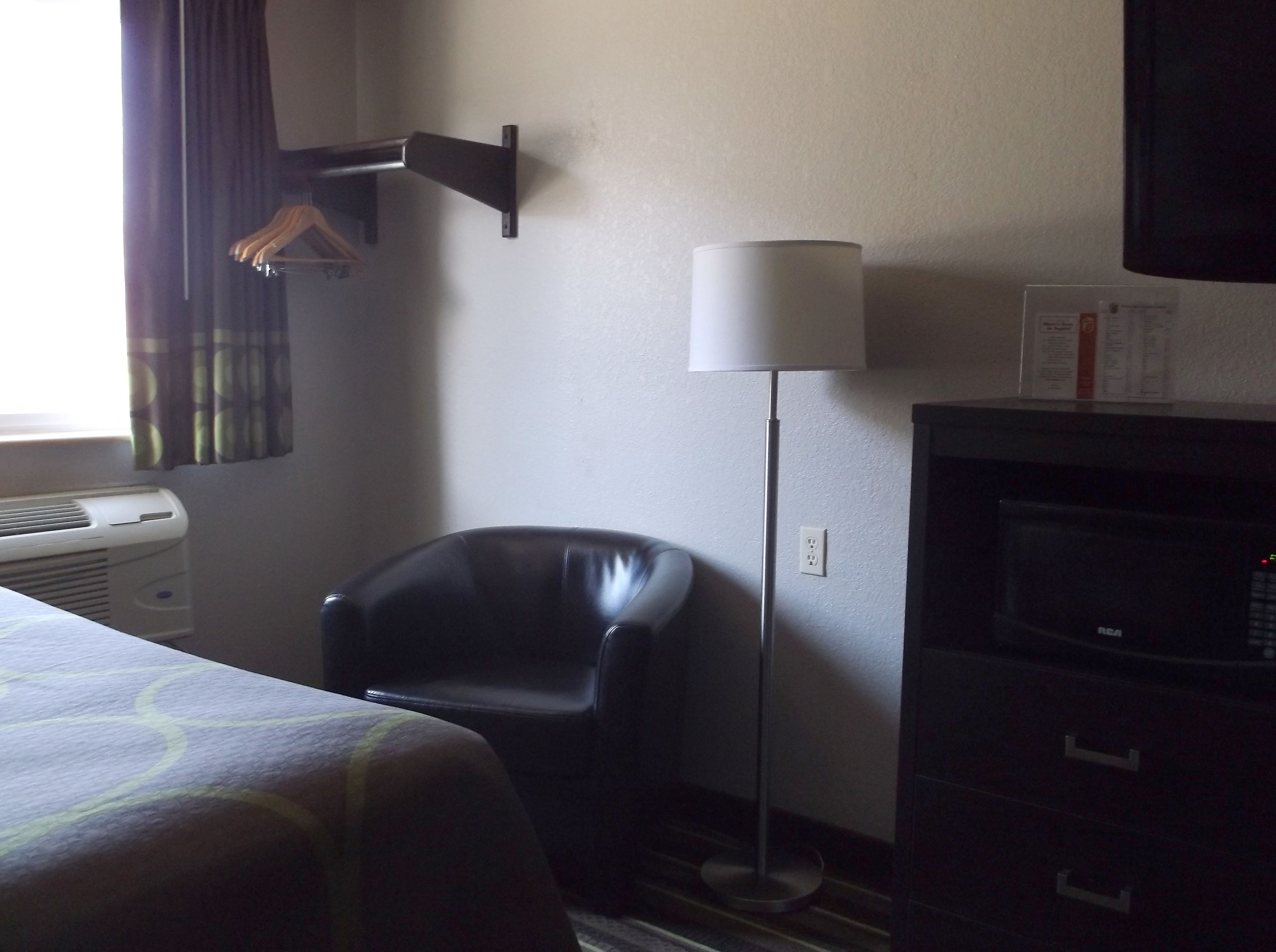 Ein Hotelzimmer mit einem Bett, einem Sessel, einer Stehlampe, einer Mikrowelle und einem Fernseher.