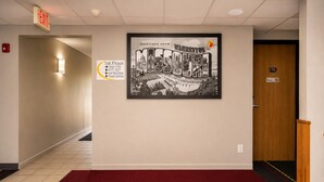 A hallway with a framed welcome sign, a red carpet, and a door marked with the number 115. - Super 8 by Wyndham Warrenton (Warrenton)
