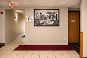 A hallway with a framed welcome sign, a red carpet, and a door marked with the number 115.