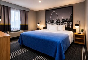 A hotel room with a large bed, a desk, a chair, a nightstand with a lamp, an air conditioner, and a cityscape view. - Super 8 by Wyndham Warrenton (Warrenton)