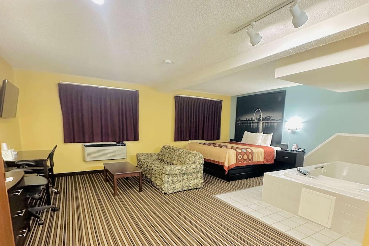 Habitación de hotel con cama, sofá, escritorio con sillas, ventana grande con cortinas, baño con bañera y un cartel de paisaje urbano en la pared.