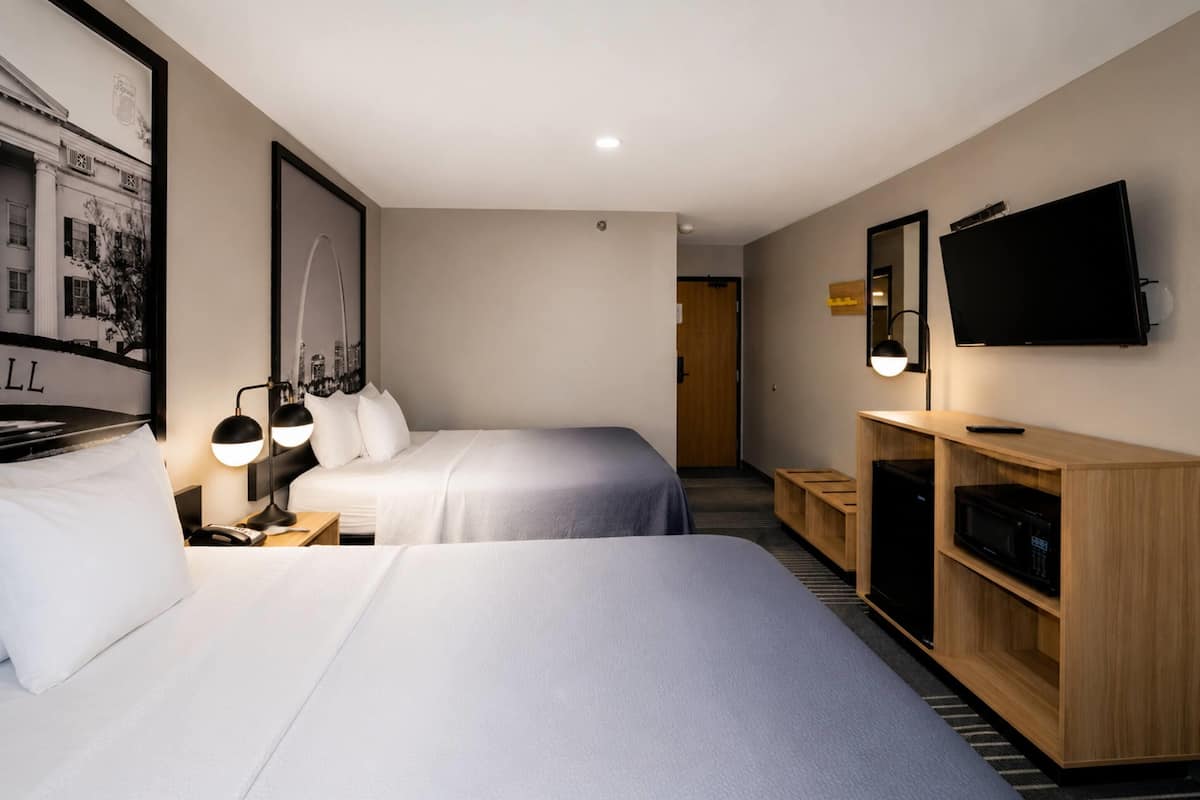 A hotel room with two beds, a TV, a desk with a lamp, and a wooden cabinet.