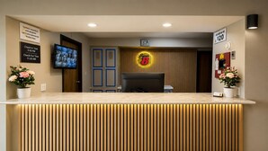 A hotel reception desk with a check-in/out time sign, a Super 8 logo, a digital clock, and a life direct no fee sign. - Super 8 by Wyndham Warrenton (Warrenton)