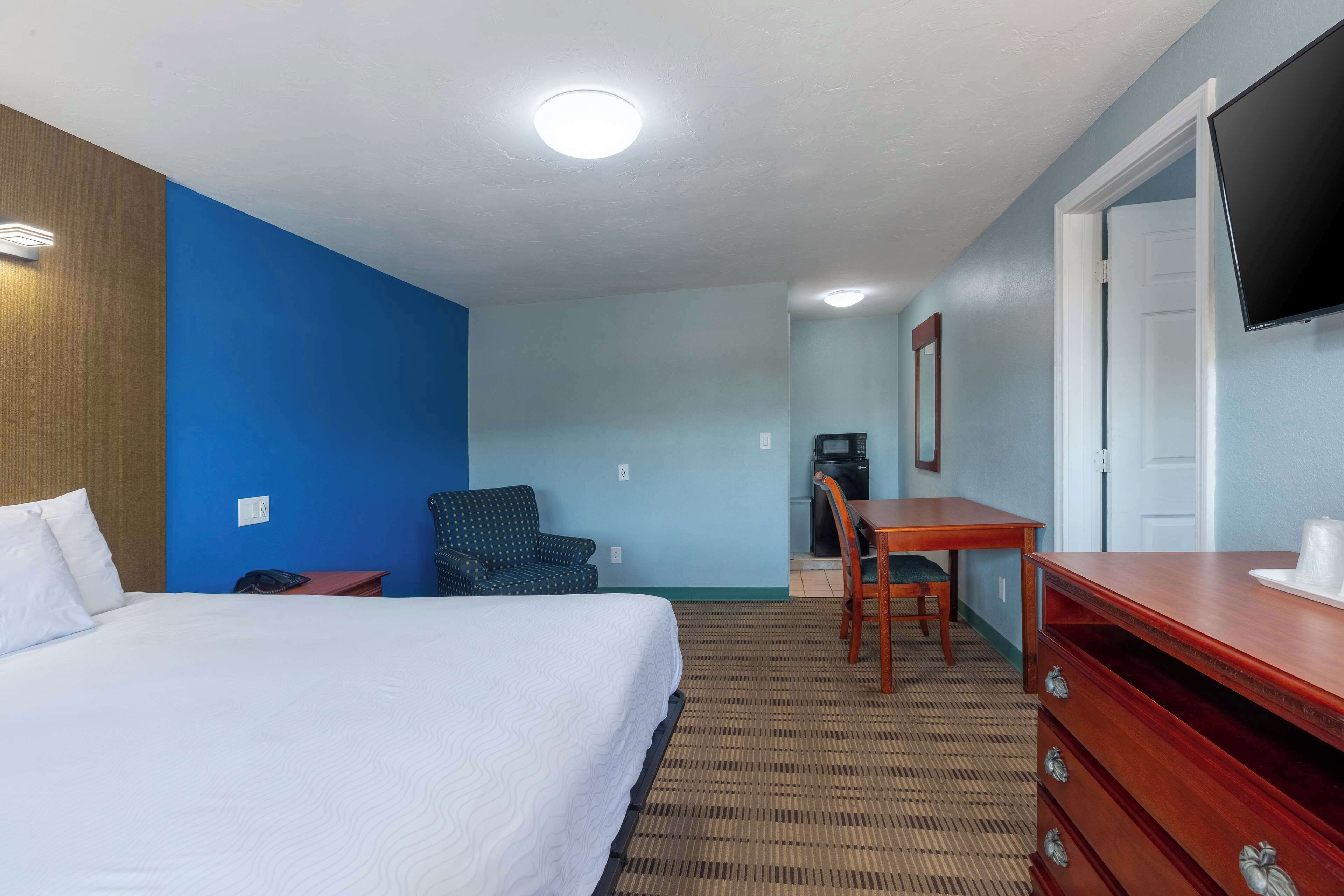 A hotel room with a bed, a desk, a chair, a dresser, and a television.