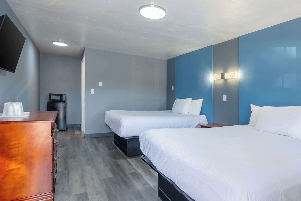 A hotel room with two beds, a wooden dresser, a TV mounted on the wall, and a trash can.