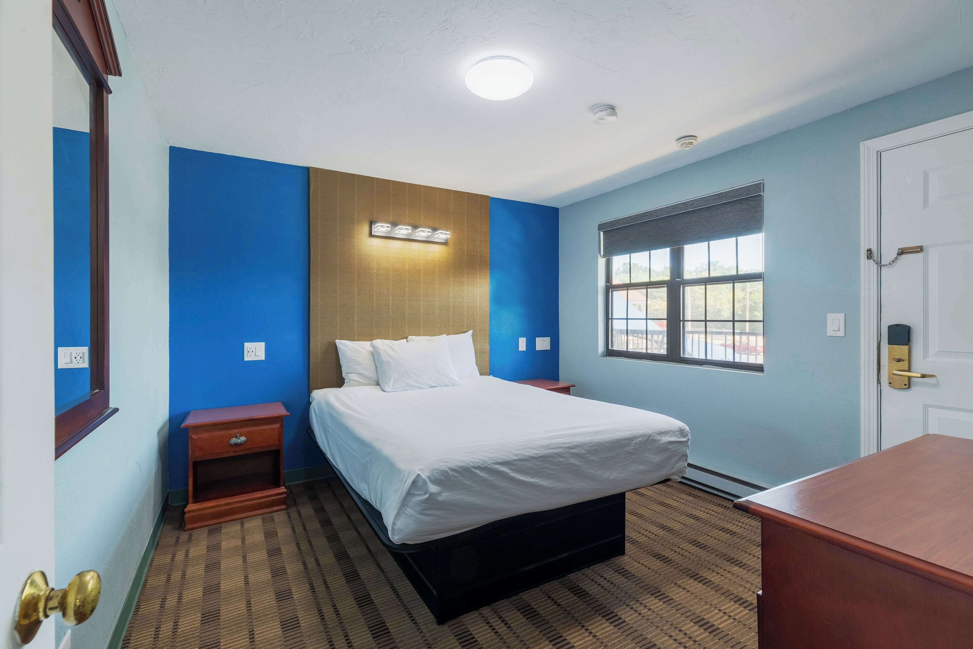 A hotel room with a bed, bedside table, and a window with blinds.