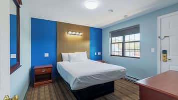 A hotel room with a bed, bedside table, and a window with blinds.