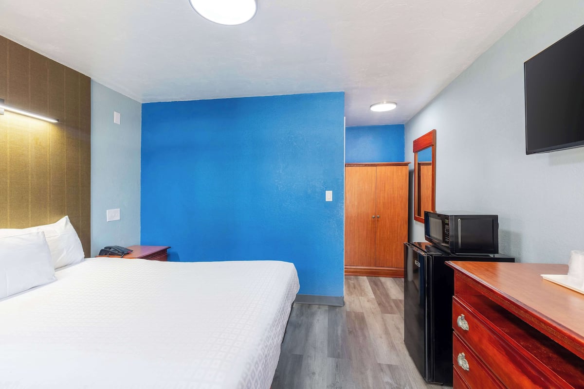 A hotel room with a bed, a desk with a computer, a microwave, and a wardrobe.