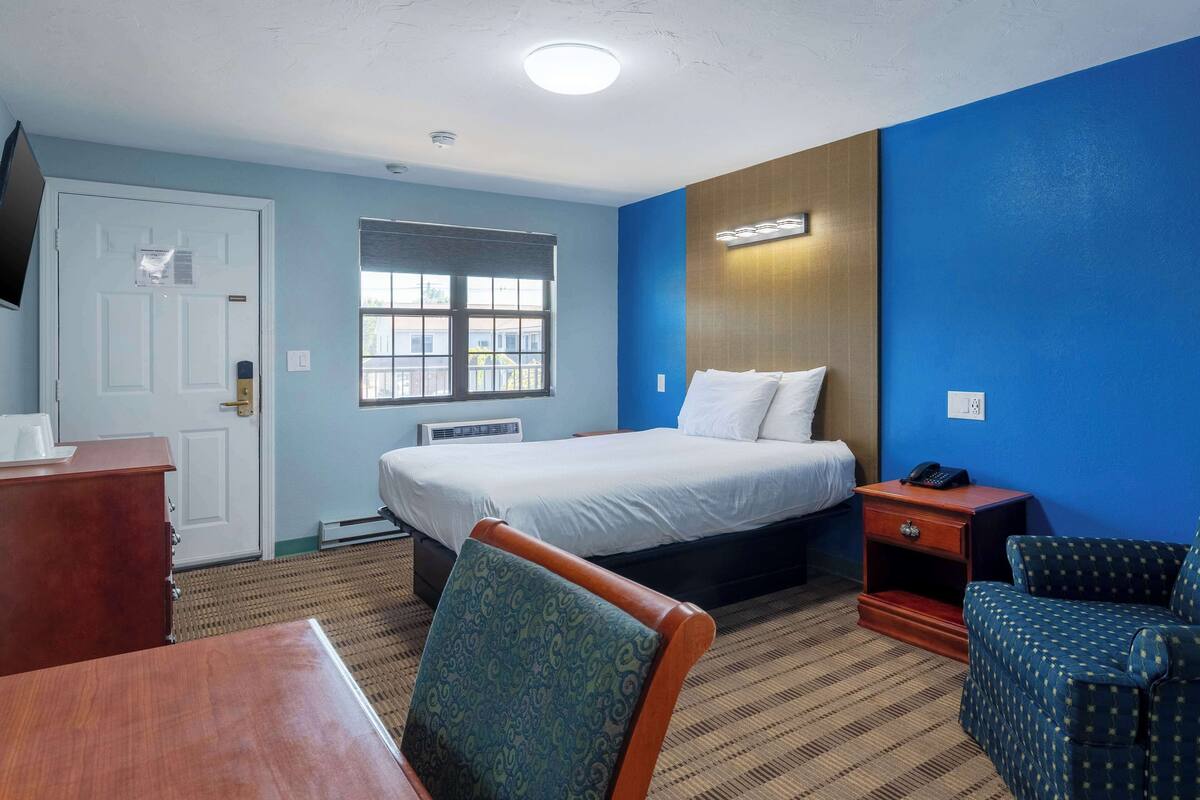 A hotel room with a bed, bedside table, chair, and a television on the wall.