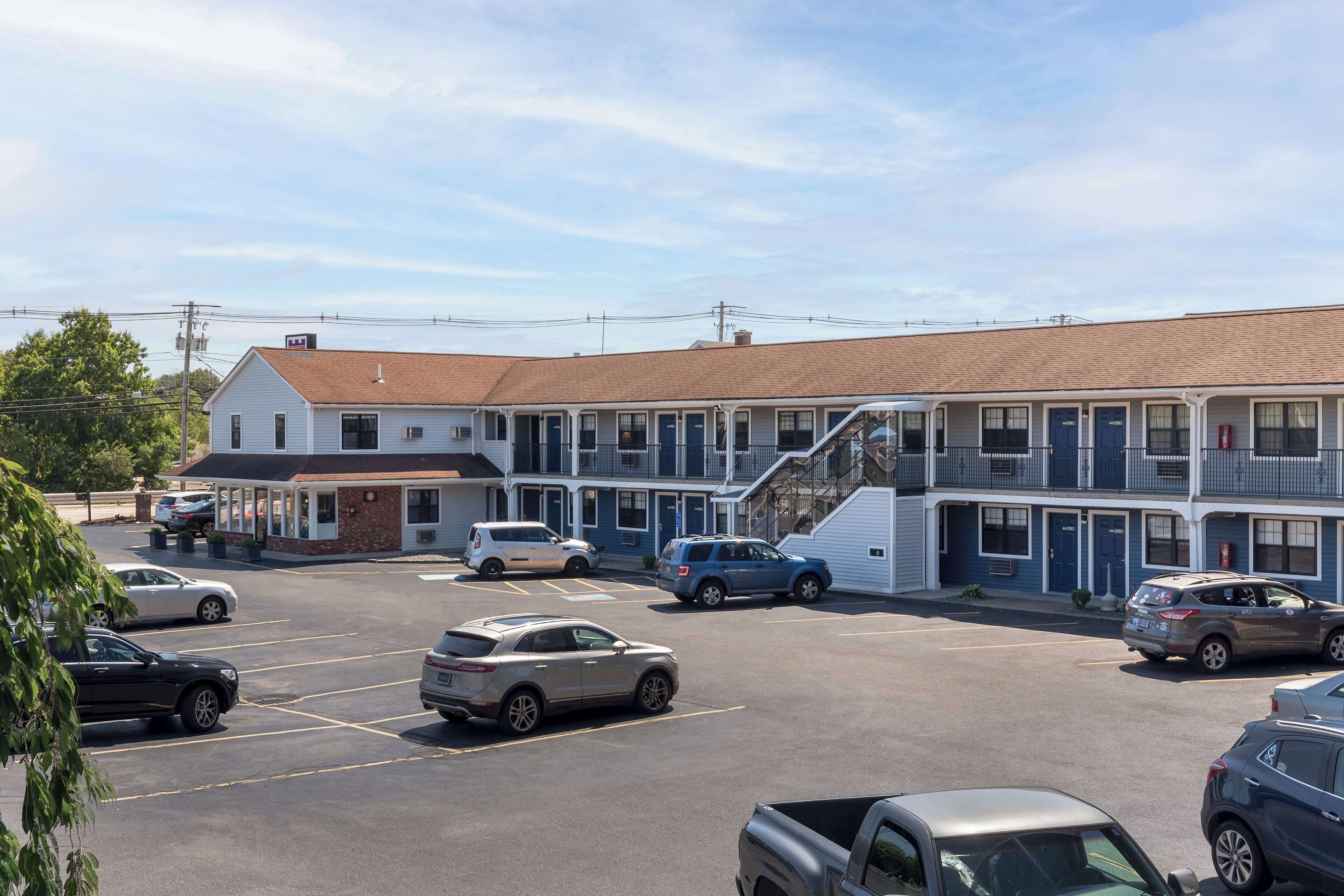 Um motel com vários quartos, estacionamento e um pequeno edifício com área coberta.