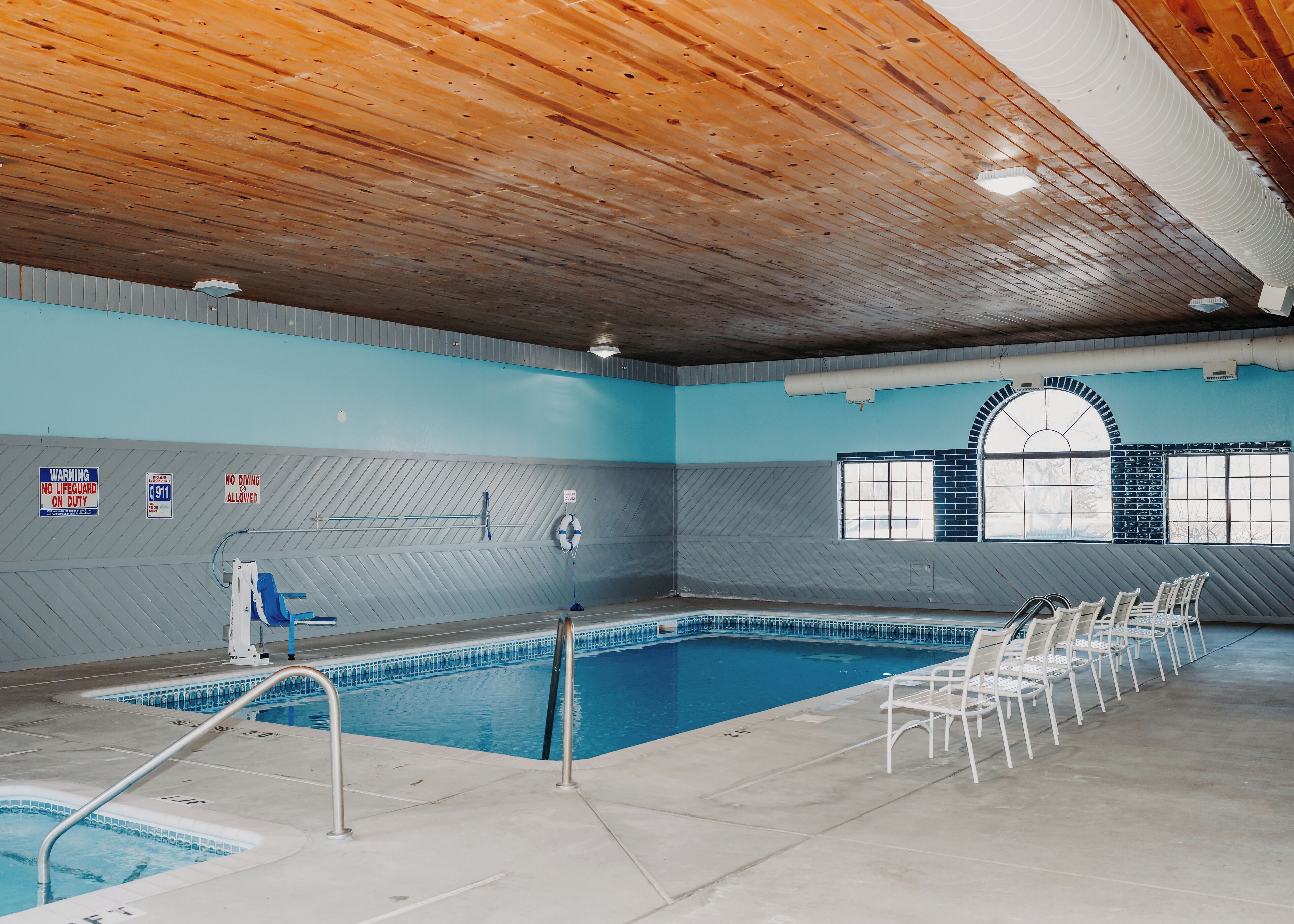 Una piscina interior con techo de madera, paredes de azulejos y una ventana con diseño de ladrillo.