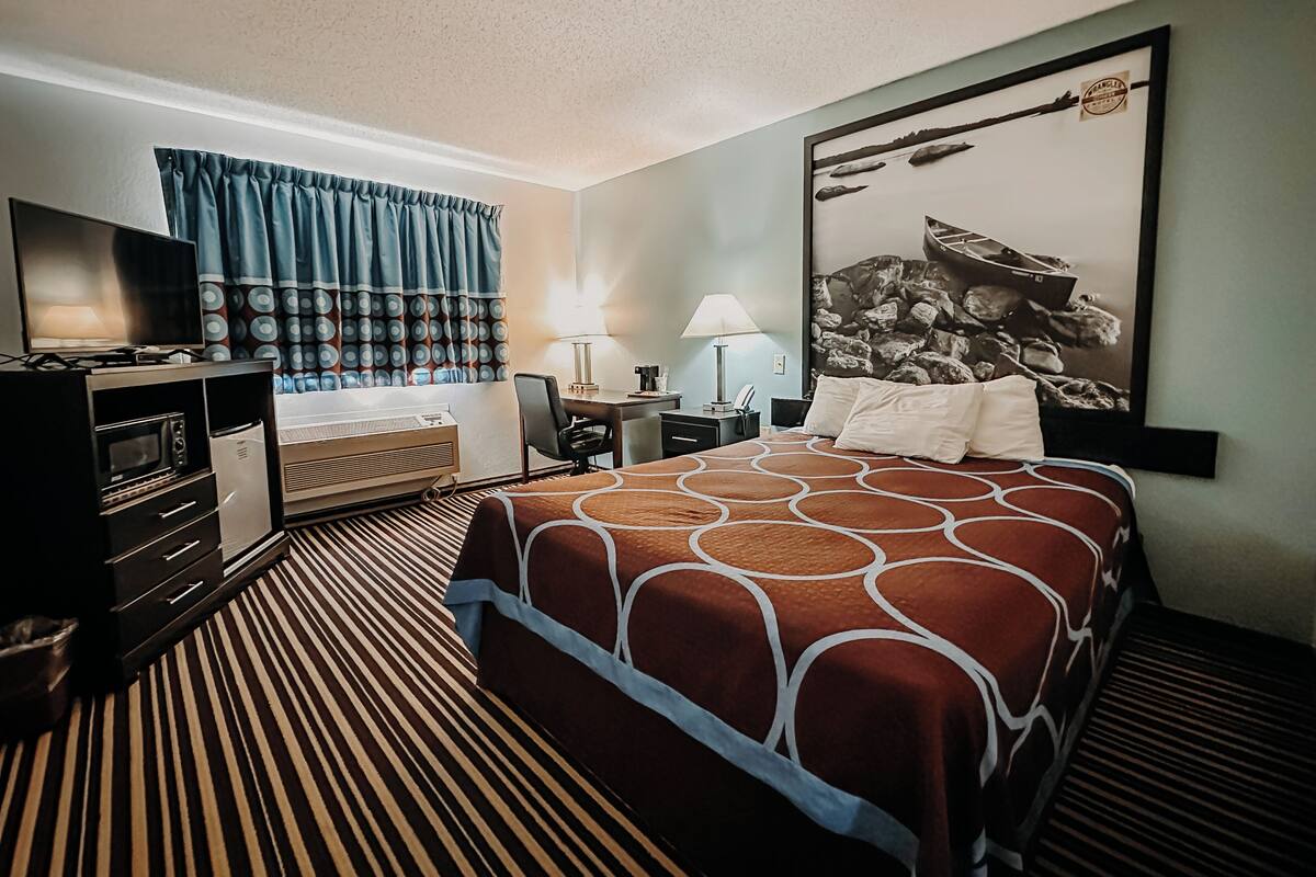 A hotel room with a bed, a desk, a chair, a television, and a window with curtains.