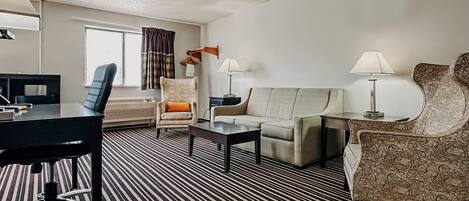 Una habitación de hotel con alfombra a rayas, un sofá, una silla, un escritorio y una lámpara.