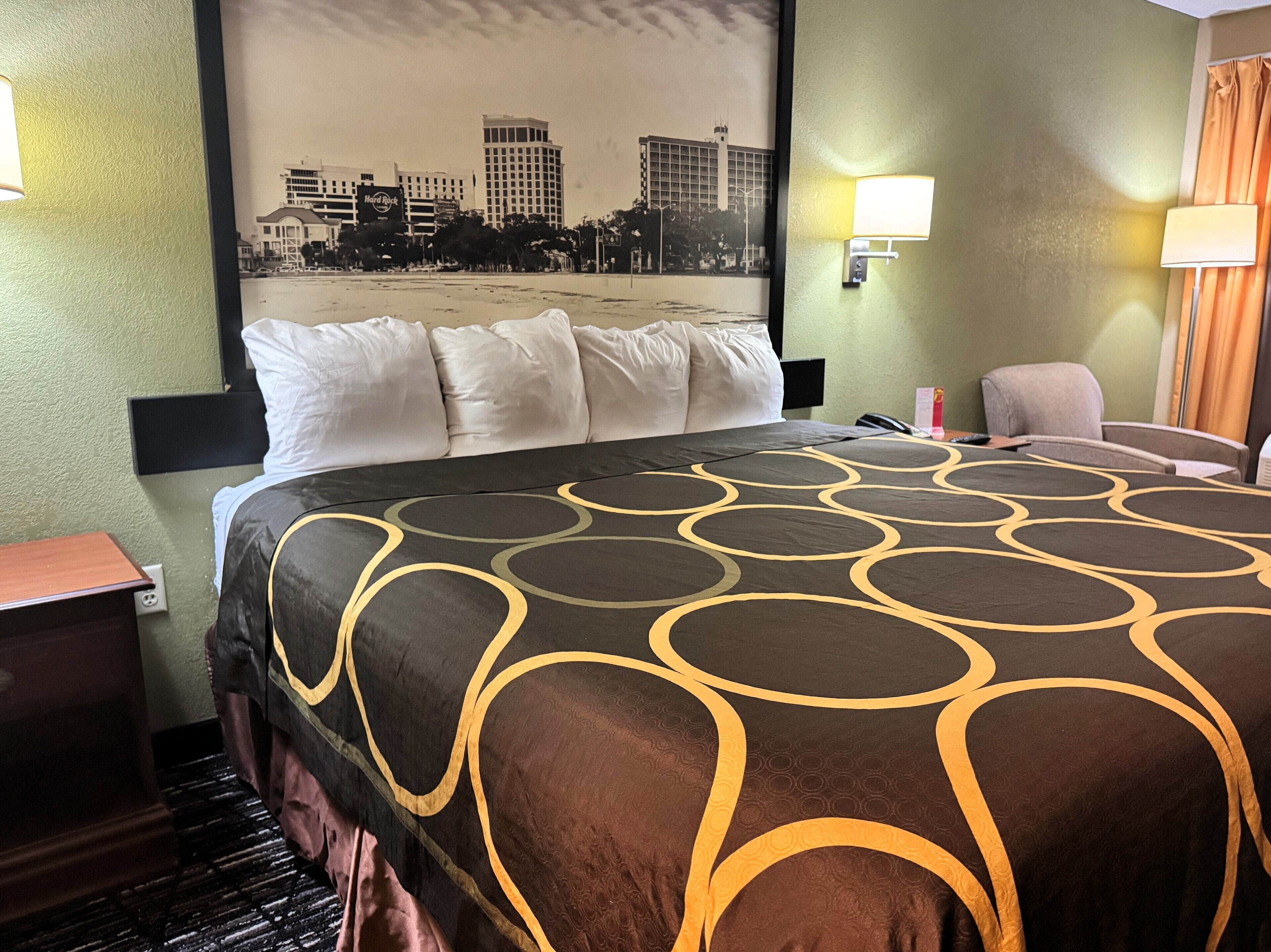 A hotel room with a bed, a cityscape poster on the wall, a desk, and a chair.