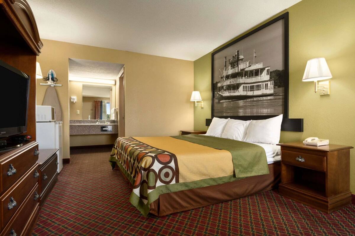 Une chambre d’hôtel avec un lit, une télévision, un bureau, une lampe et un tableau au mur.