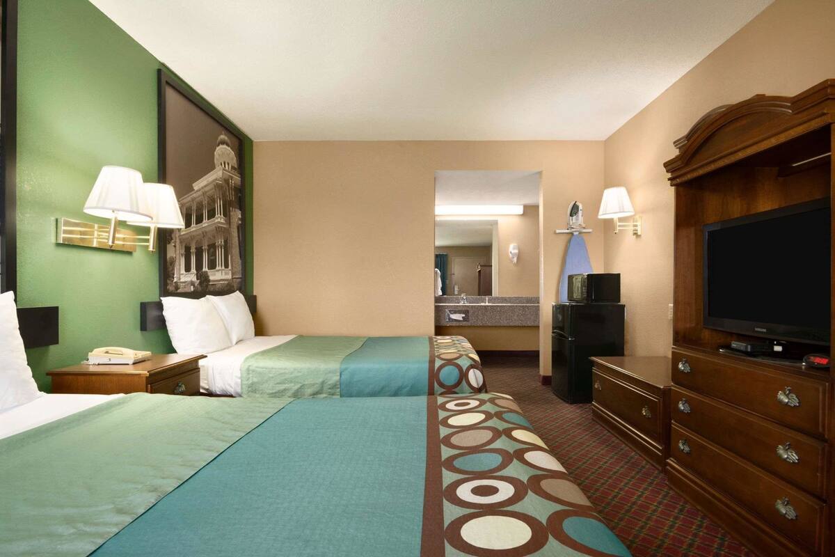 Une chambre d’hôtel avec deux lits, une télévision, un réfrigérateur, un bureau avec un téléphone et une salle de bain visible à travers une porte ouverte.