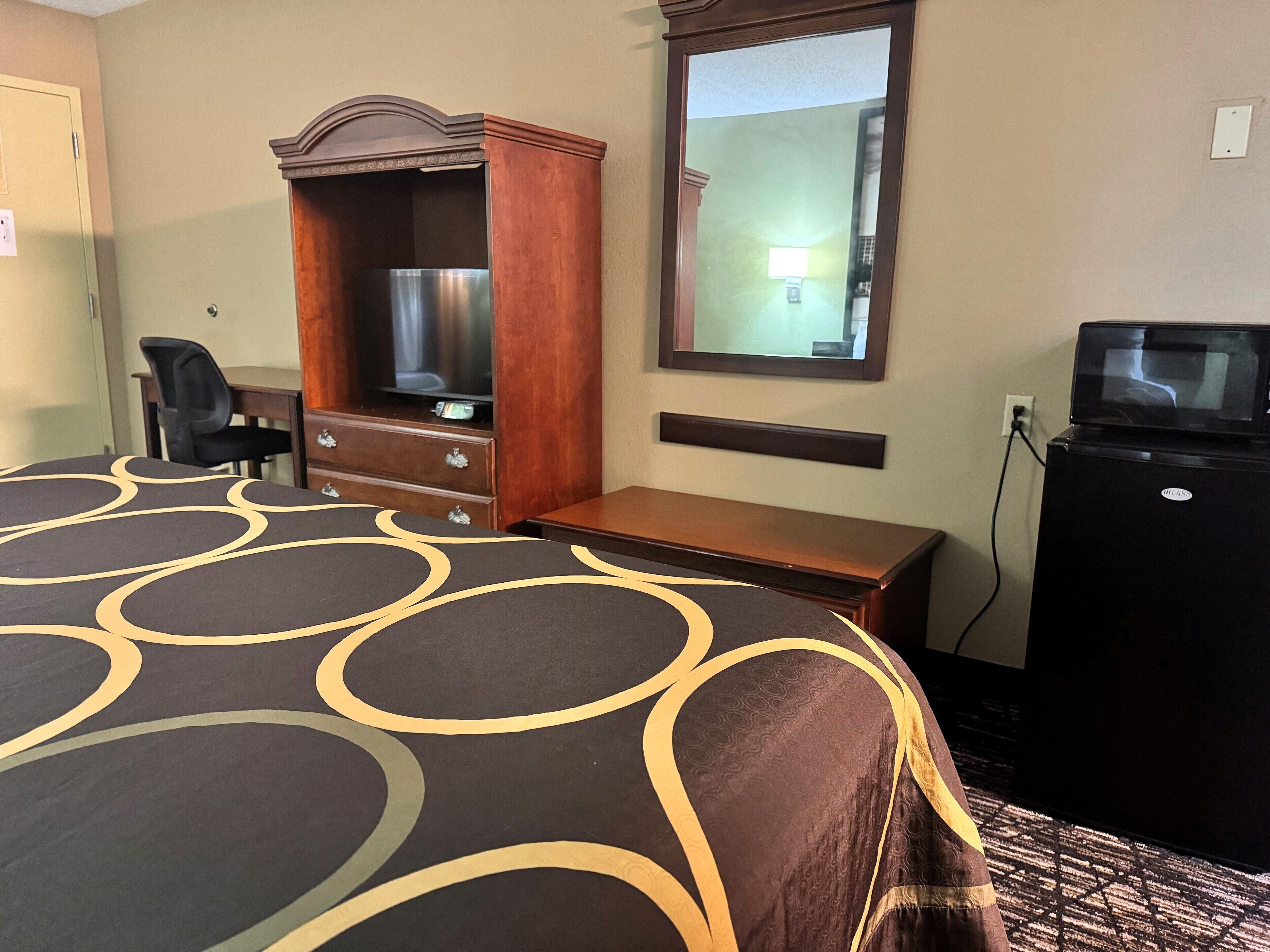 Une chambre d’hôtel équipée d’un lit, d’un bureau, d’une commode, d’une télévision et d’un four à micro-ondes.