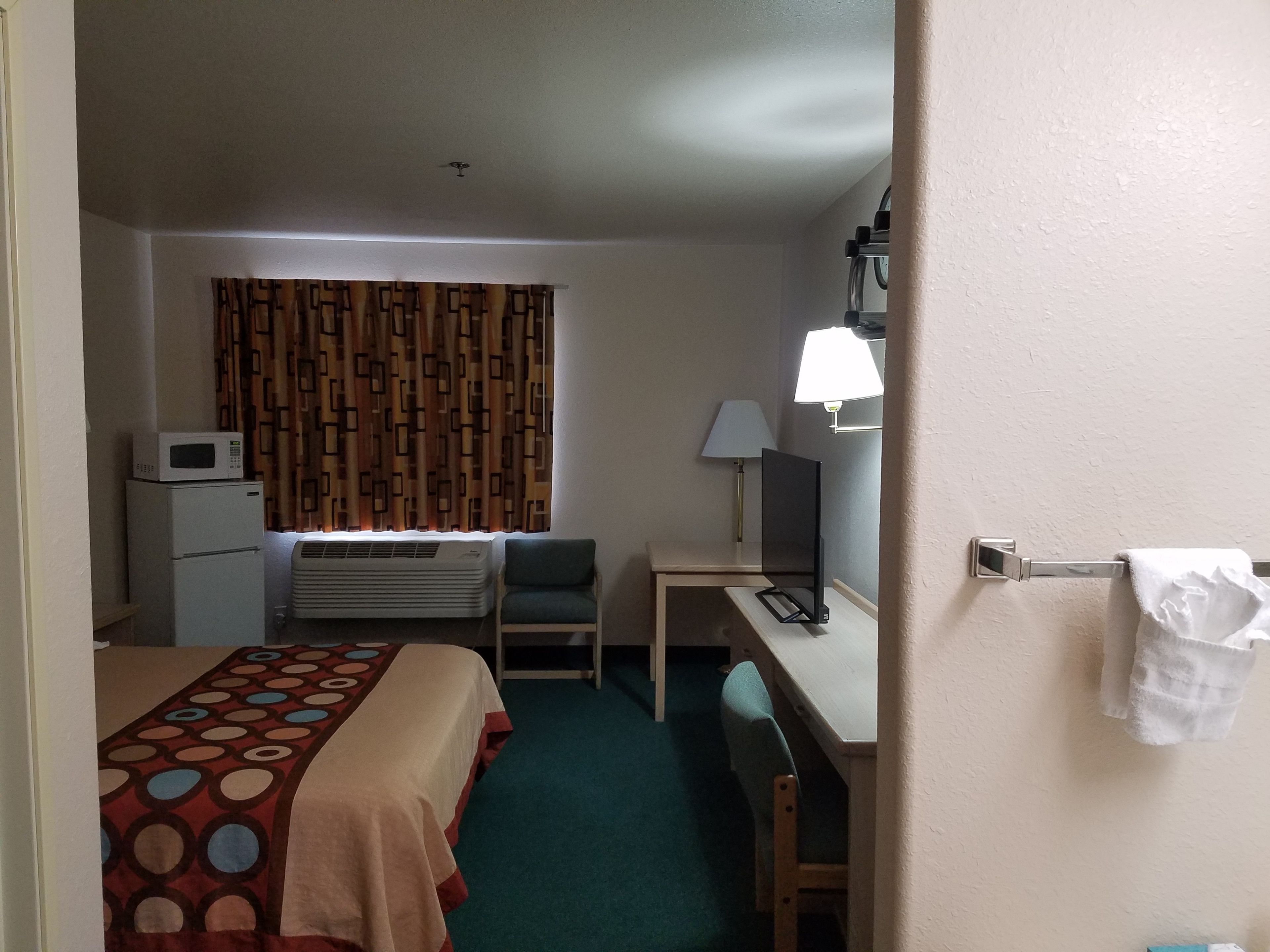 Habitación de hotel con cama, escritorio, silla, televisor, lámpara, microondas y aire acondicionado.