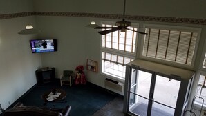 A living room with a television, a ceiling fan, a chair, a small table, and a window with blinds.