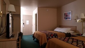 A hotel room with two beds, a desk with a lamp, a mirror, and a painting on the wall.