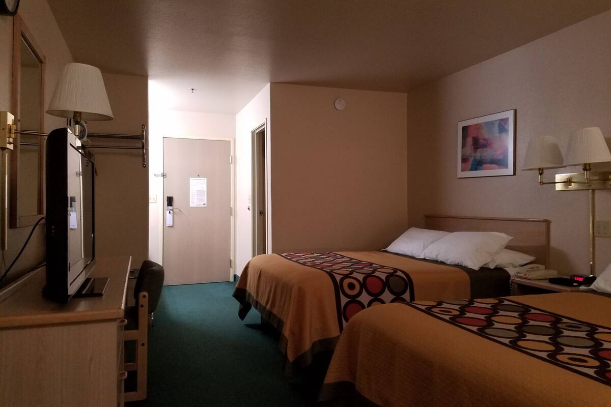 Quarto de hotel com duas camas, uma escrivaninha com luminária, um espelho e um quadro na parede.